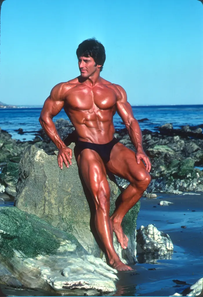 Vivid color and professional lighting capture a deep tan against ocean rocks and blue sky.