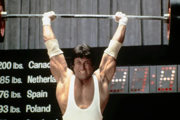 A gritty in-competition weightlifting shot with the scoreboard visible captures rare unposed action.
