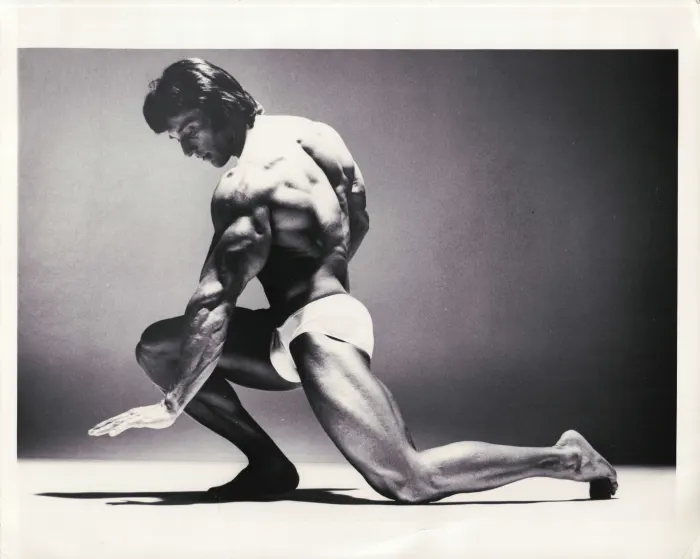 An immaculately lit kneeling-lunge pose from a Richard Avedon-style studio shoot, dramatic side lighting and negative space.