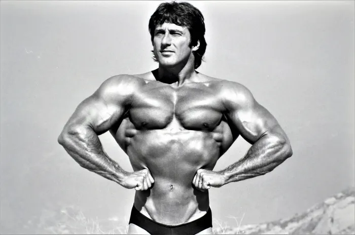 A tight, magazine-quality crop of a front double-biceps pose in the desert, striking contrast and intense expression.