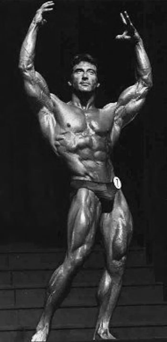 A dynamic overhead victory pose on the stage steps at a 1983 Olympia-era event.