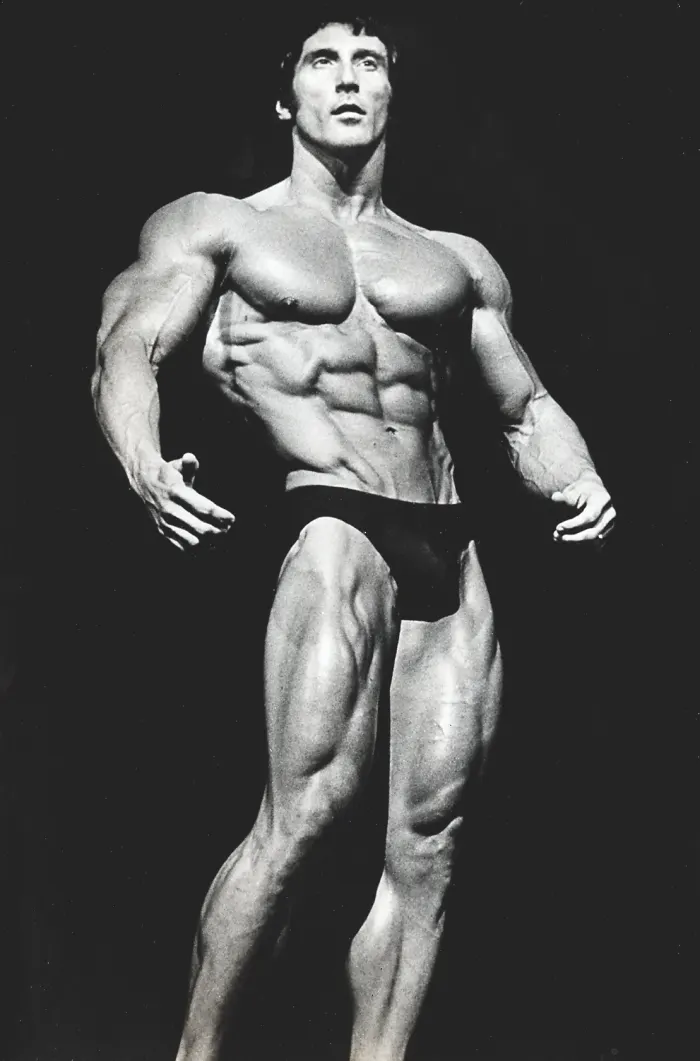 Dramatic low-key lighting on a perfectly symmetrical standing physique pose against black.