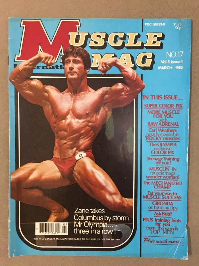 A MuscleMag International 'three in a row!' cover with a dynamic seated double-biceps pose.