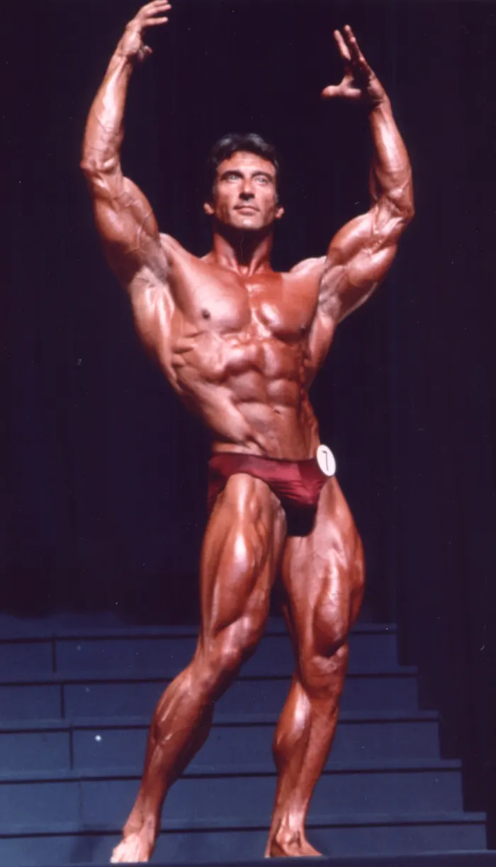 Color on-stage documentation, competitor number visible, arms raised in a triumphant V-pose.