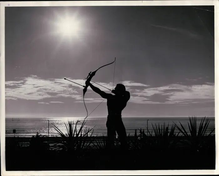A full silhouette drawing a longbow against a blazing sun over the ocean, cinematic and entirely unique.