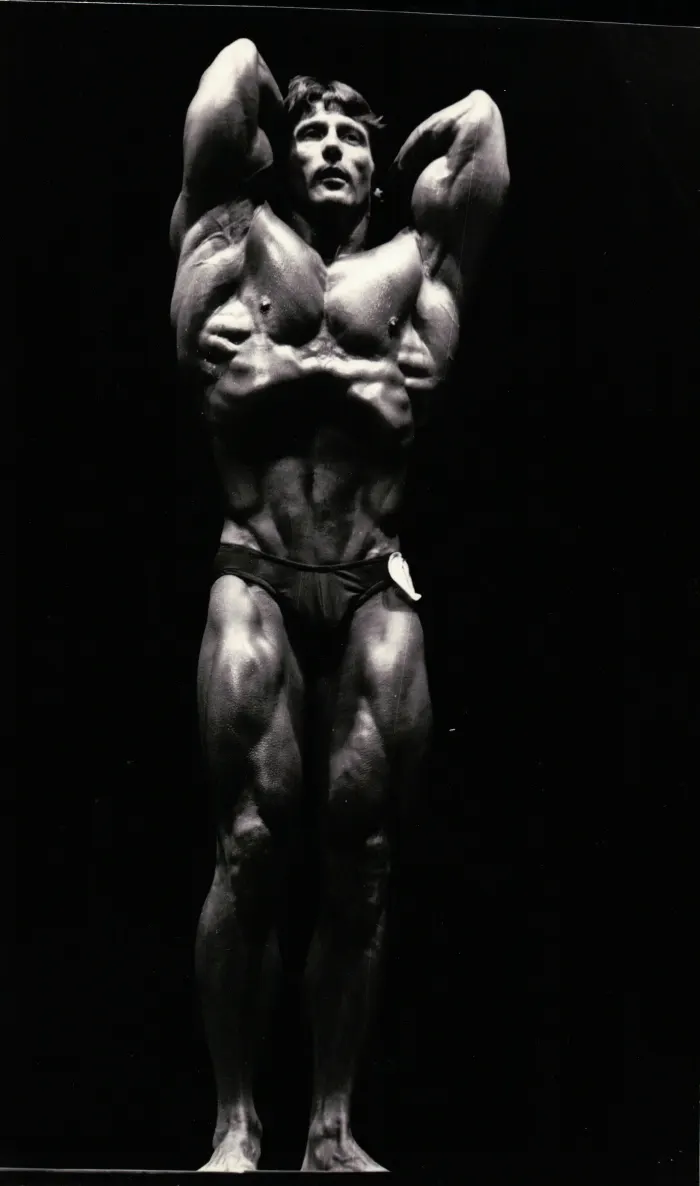 A high-resolution wide stage view of the signature vacuum pose, judging tag visible, dramatic black-background lighting.